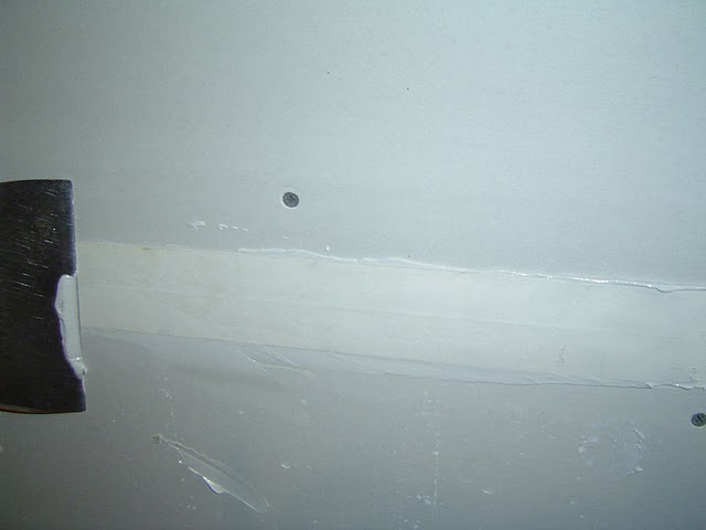 Apply the mudded side of the drywall tape to the joint and draw a drywall taping knife over the surface of the tape.